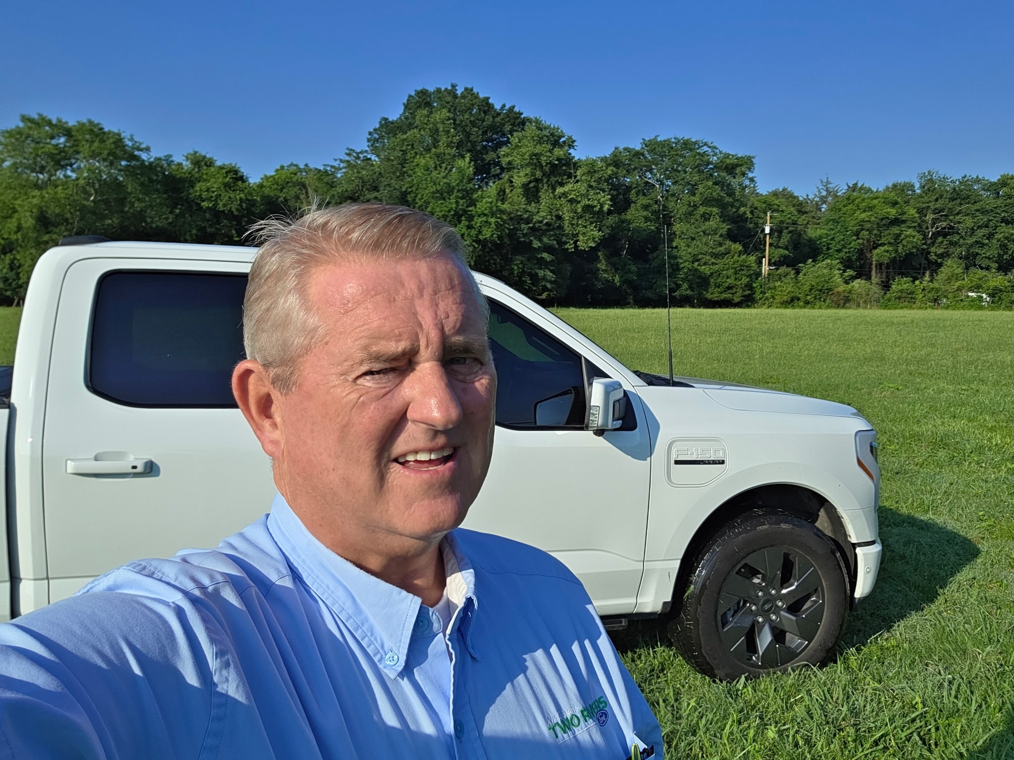 A man takes a selfie in front of his white F-150 Lightning truck.